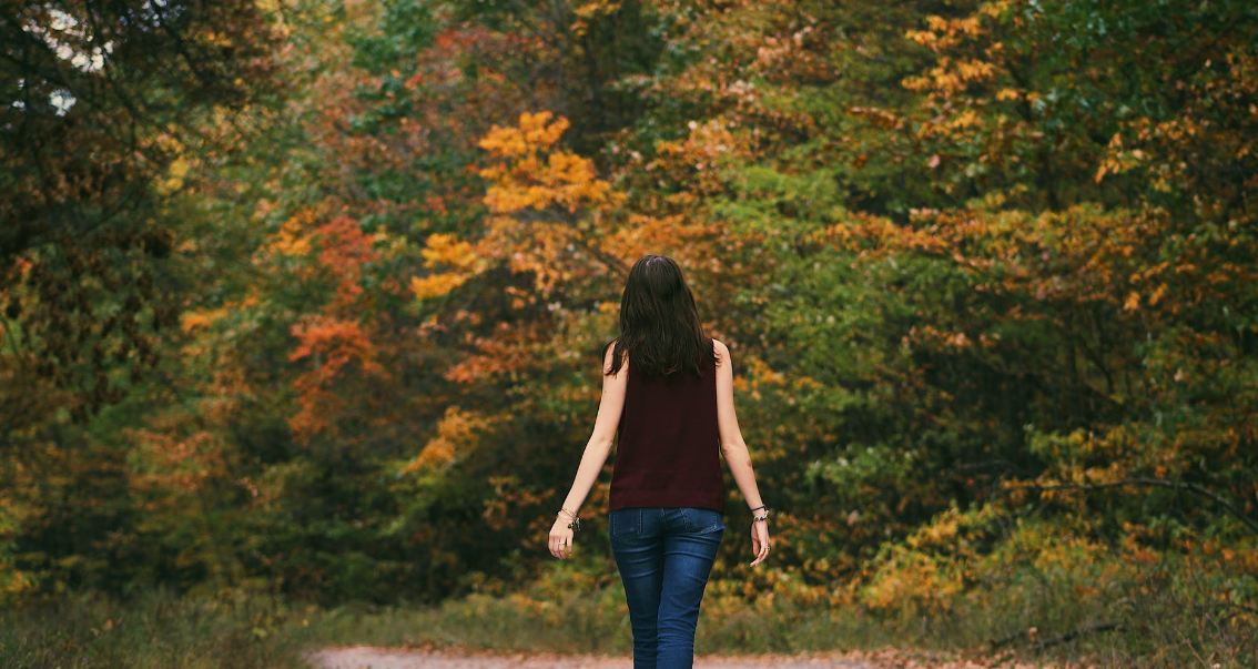 woman-in-brown-sleeveless-dress-and-blue-jeans-standing-on-gray-path-road