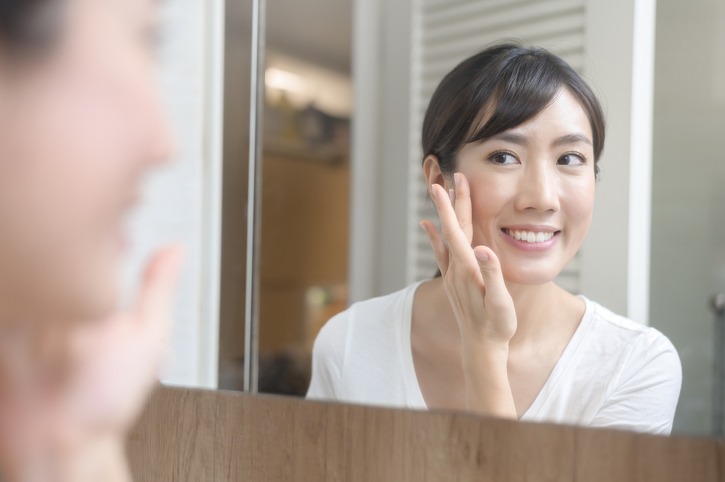 Happy beautiful woman applying moisturizing cream on face, skin care and treatment concept