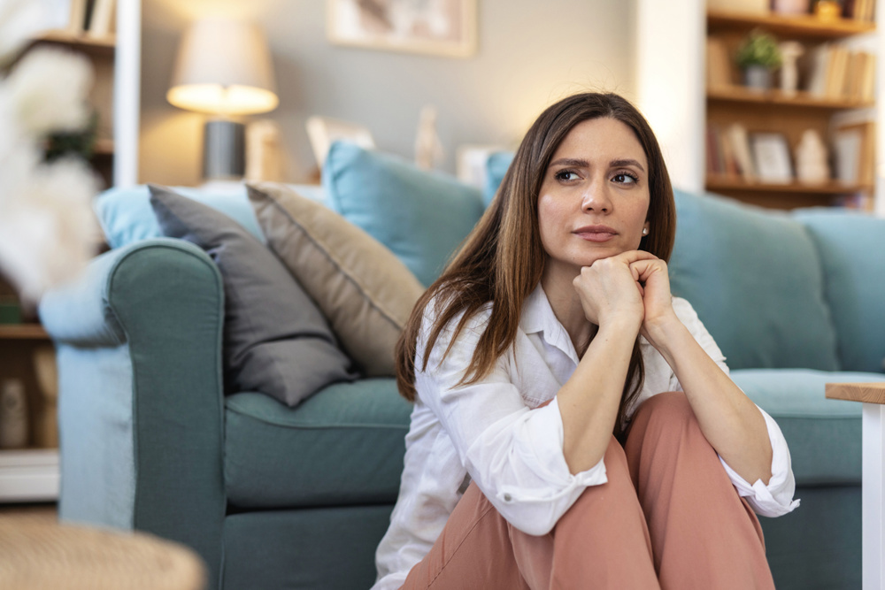 Thinking, sad and woman in home on the floor with anxiety for issue, depression and reflection in living room. Apartment, morning and thoughtful person with worry, overthinking and wondering in house