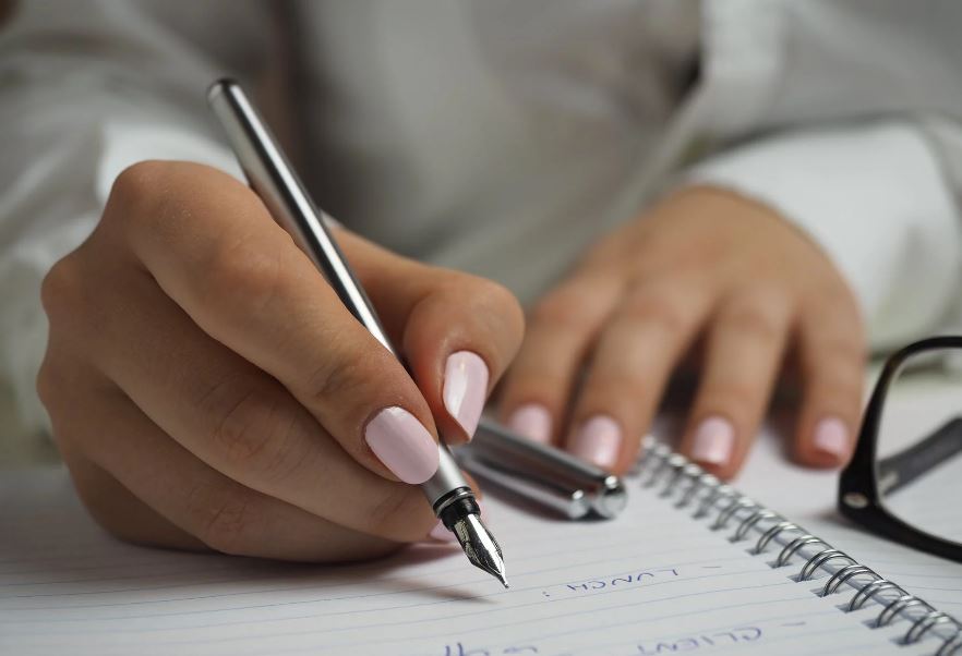 a close up of a person holding a pen and writing on a notebook