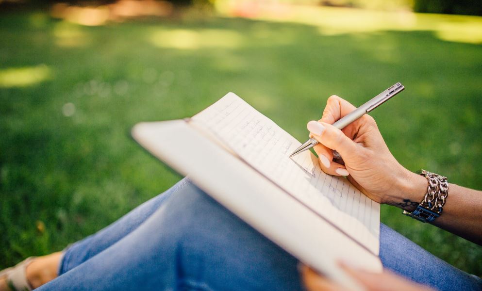 a person sitting on the grass writing in a notebook