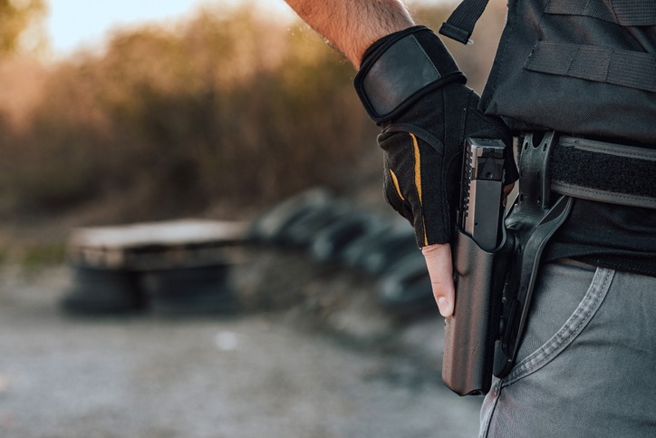 Close-up image of a man holding hand gun in holster on the belt.